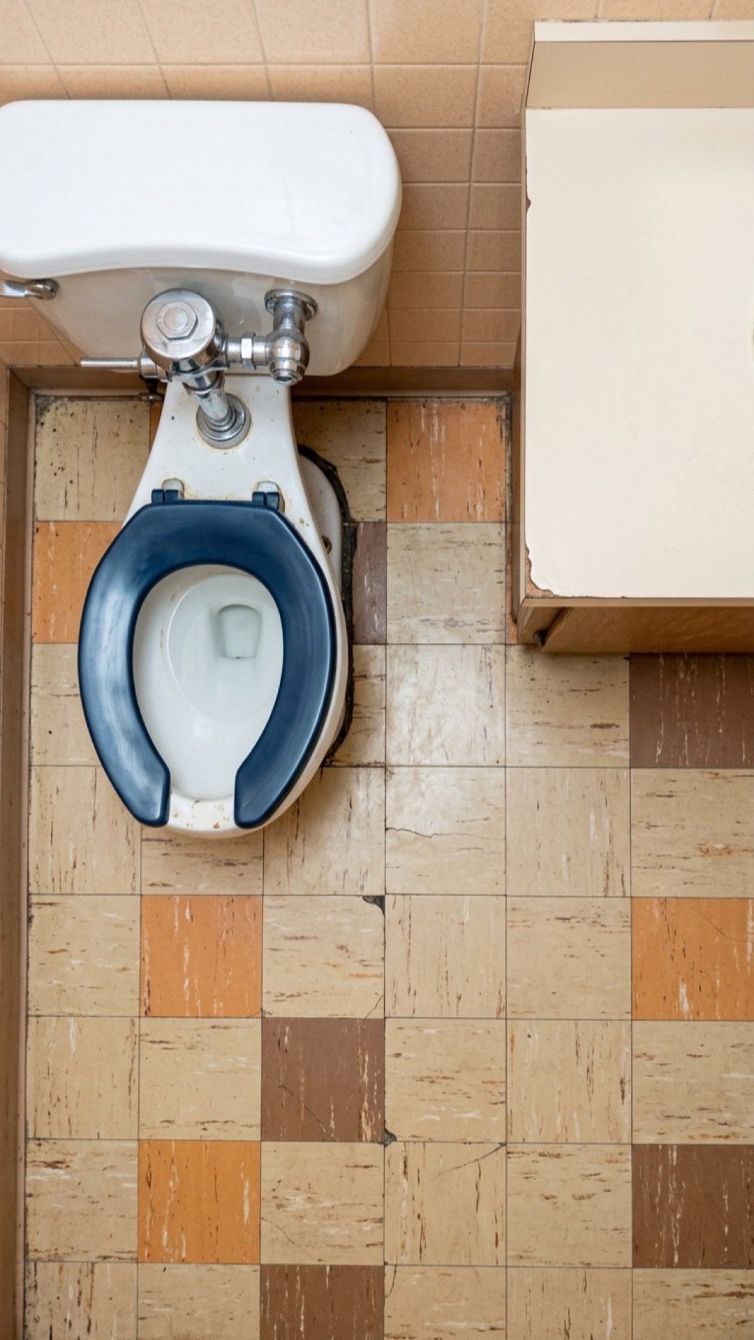 Looking down at an old buffet bathroom: a toilet with a blue seat and a tiled floor.